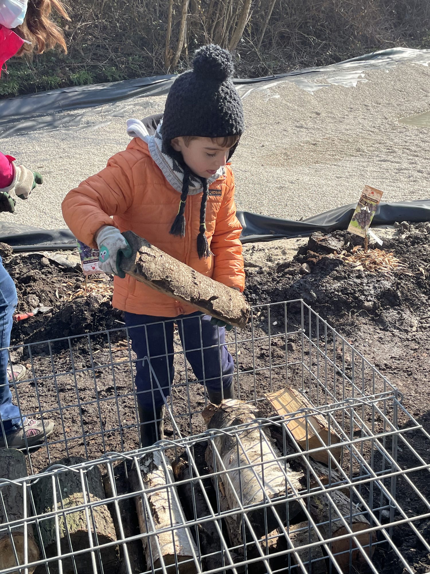 Jardin biodiversité - un enfant qui rempli un banc de rondins de bois